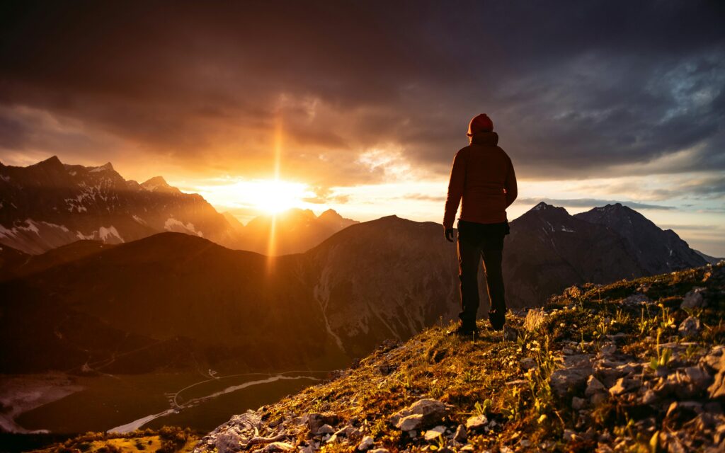 A hiker enjoys a breathtaking sunset view over the dramatic Alpine mountain range.